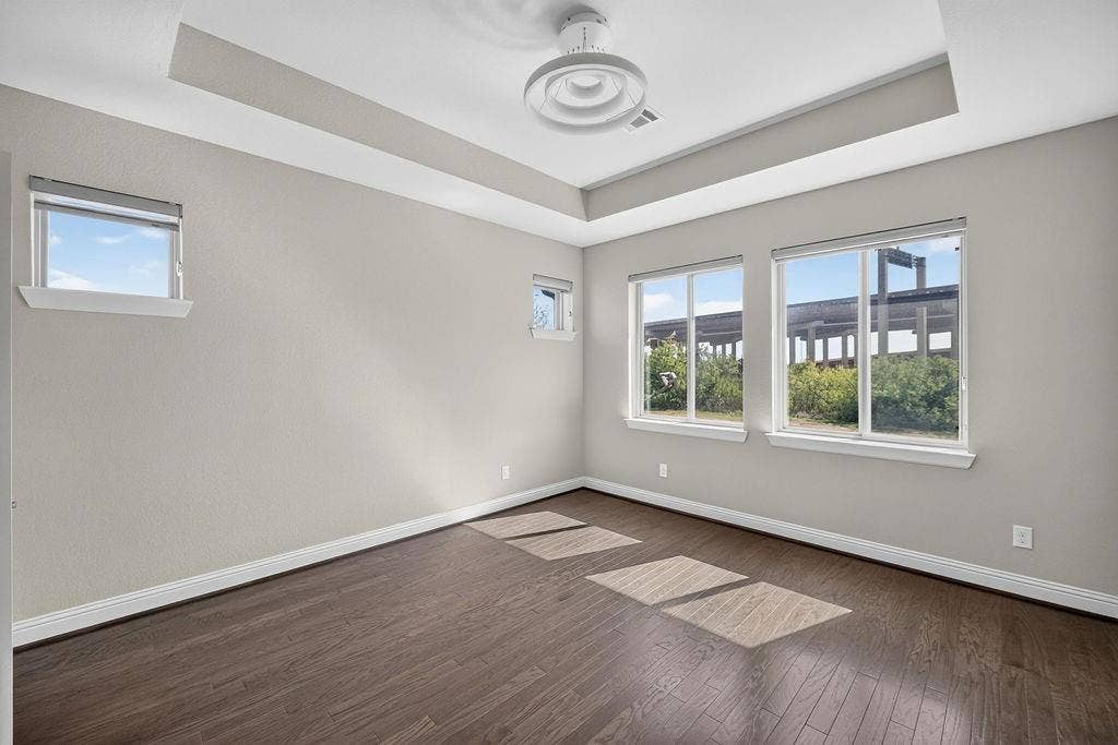 Tray ceiling, dark wood-finish flooring, multi-pane windows, and modern flush-mount overhead lighting