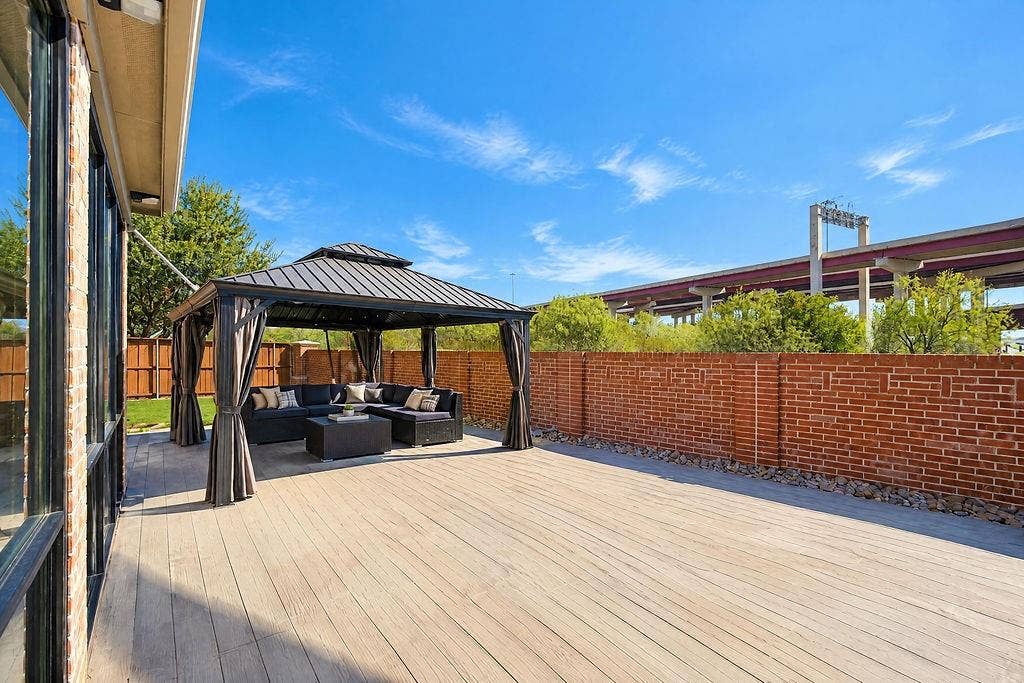 Covered patio featuring brick exterior walls, wood-finish tile flooring, large multi-panel glass sliding doors, recessed ceiling lighting, and a black ceiling fan
