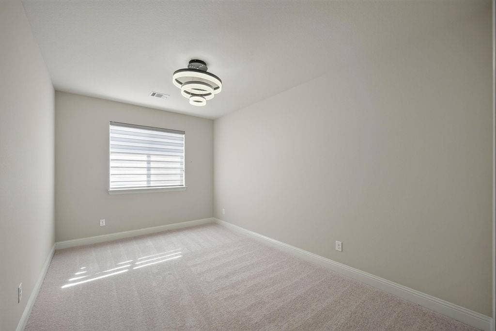 Neutral-toned interior featuring wall-to-wall carpeting, a contemporary tiered flush-mount light fixture, and a window with horizontal shades