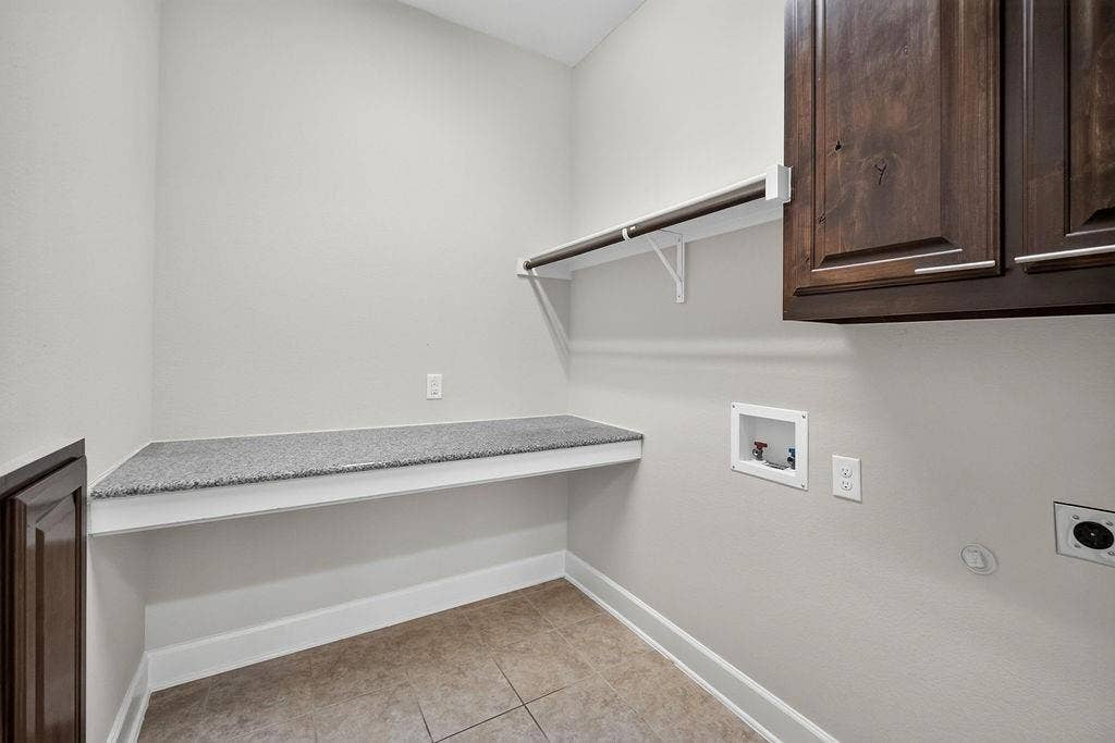 Laundry area featuring dark wood-finish upper cabinetry, a stone-composite folding counter, and a built-in wall-mounted hanging rod over tile flooring