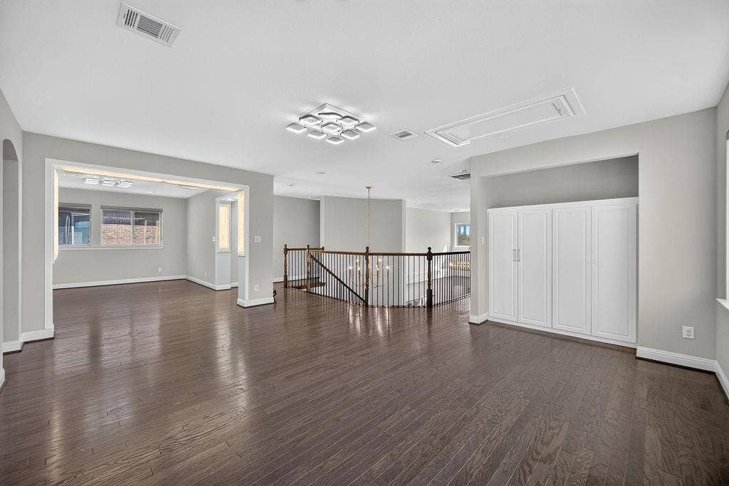 Open-concept area featuring wood-finish flooring, built-in cabinetry, tiered modern ceiling lighting, and a balustrade staircase