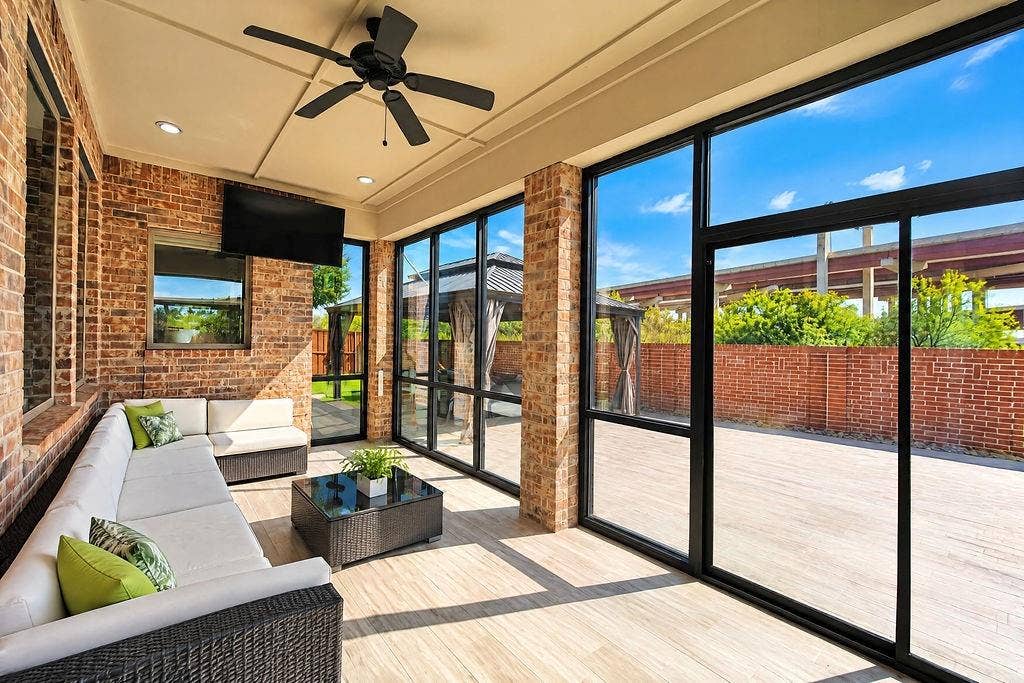 Enclosed patio featuring exposed brick walls, expansive black-framed windows, wood-finish flooring, and a ceiling-mounted fan