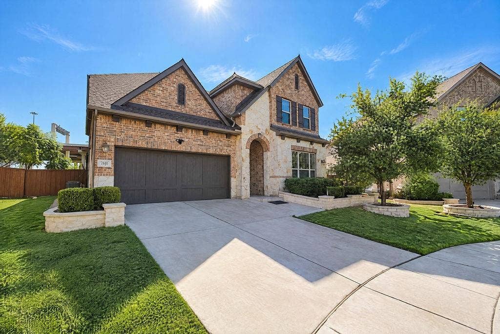 Multi-level exterior featuring a brick and stone facade, arched entryway, attached garage, and stone-bordered landscaping beds
