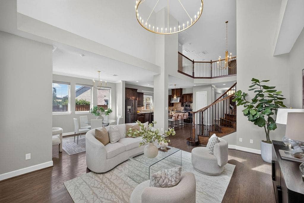 Double-height ceilings, dark wood-finish flooring, staircase with wood and metal balusters, oversized circular chandelier, and custom dark-toned cabinetry