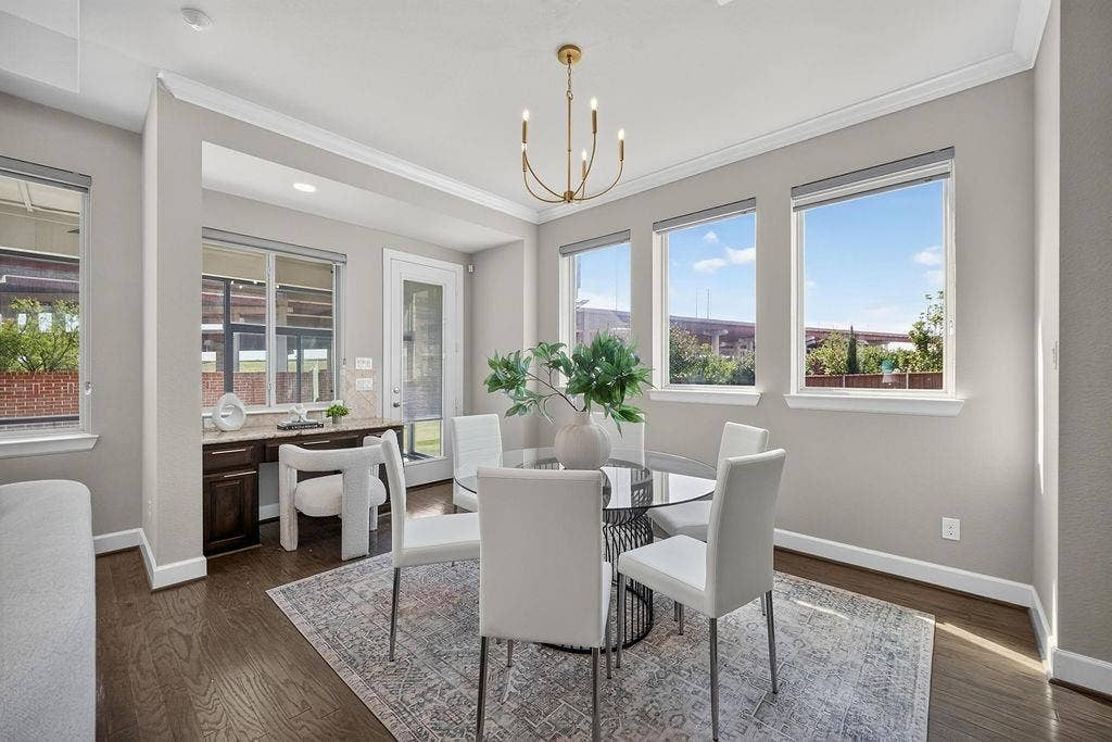 Wood-finish flooring, built-in desk with stone countertop, multi-light chandelier, and large windows with crown molding
