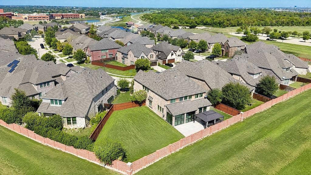 Aerial perspective featuring a multi-story residence with a concrete patio, wood-style privacy fencing, and expansive green space