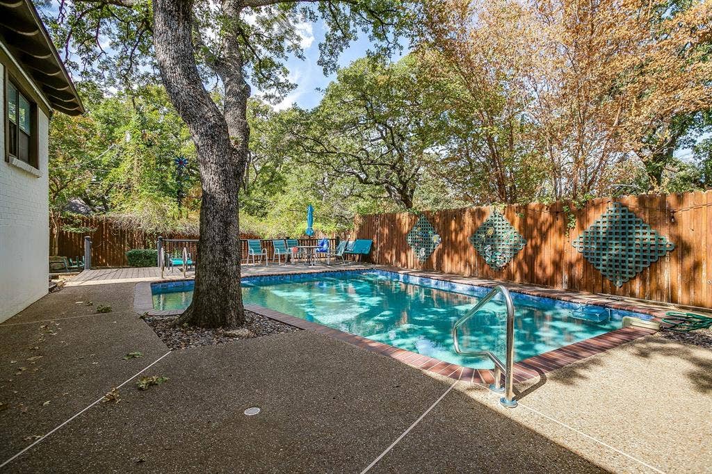 Swimming pool with brick coping, surrounding aggregate concrete patio, and mature trees