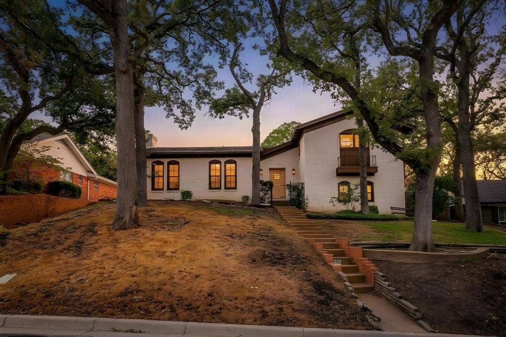 White stucco exterior with brown trim details, arched windows, and a second-story balcony