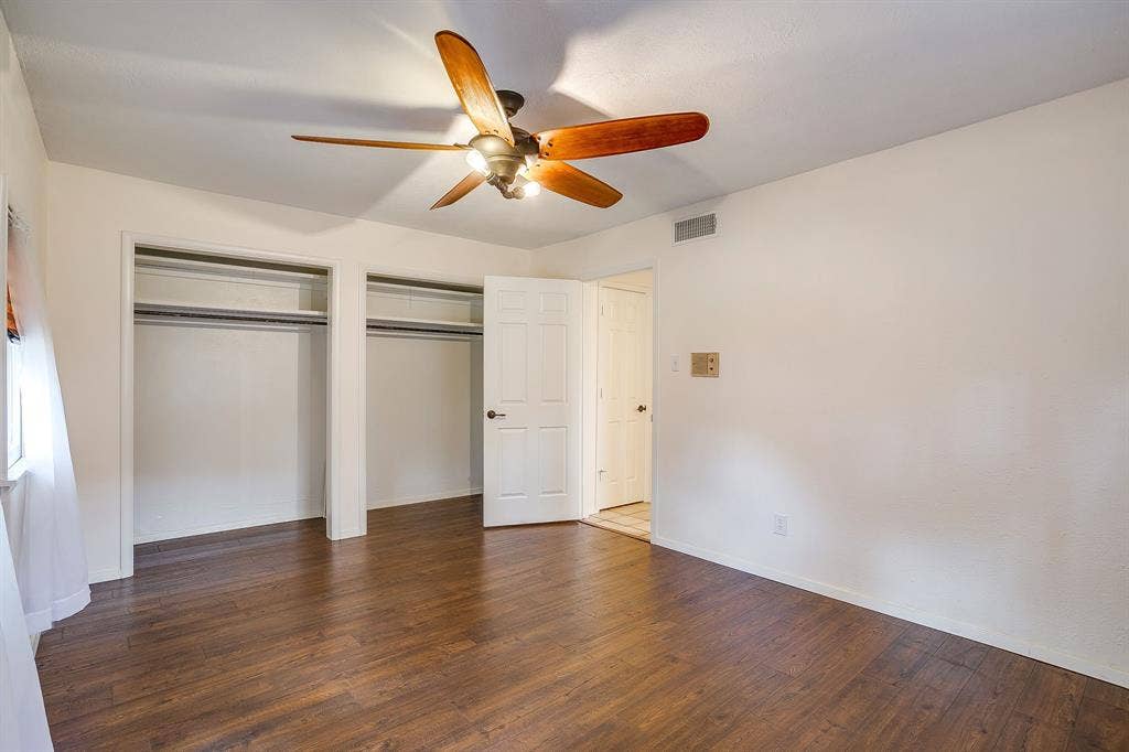 Wood-finish flooring, ceiling fan with integrated lighting, two built-in closets with shelving and hanging rods, and a white paneled door