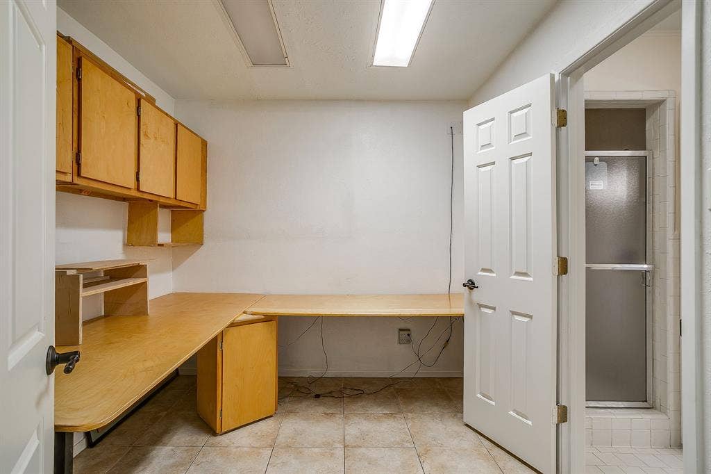 Built-in L-shaped desk with overhead cabinetry, tiled flooring, and a shower enclosure with a frosted glass door