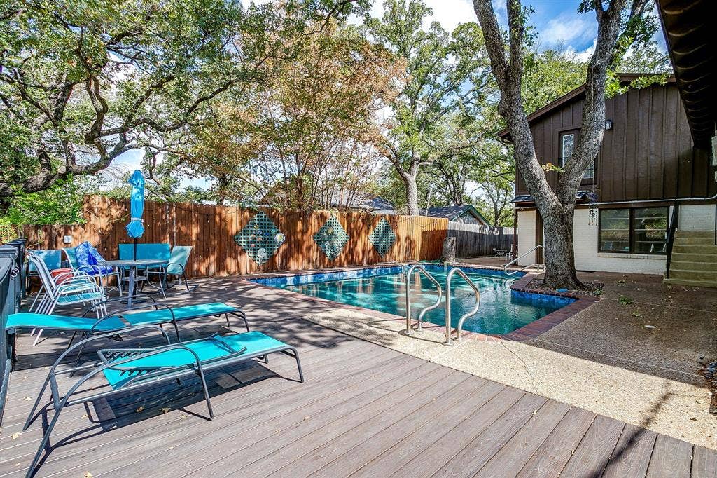 Expansive wood-finish deck with an in-ground swimming pool, surrounded by a wood privacy fence and mature trees