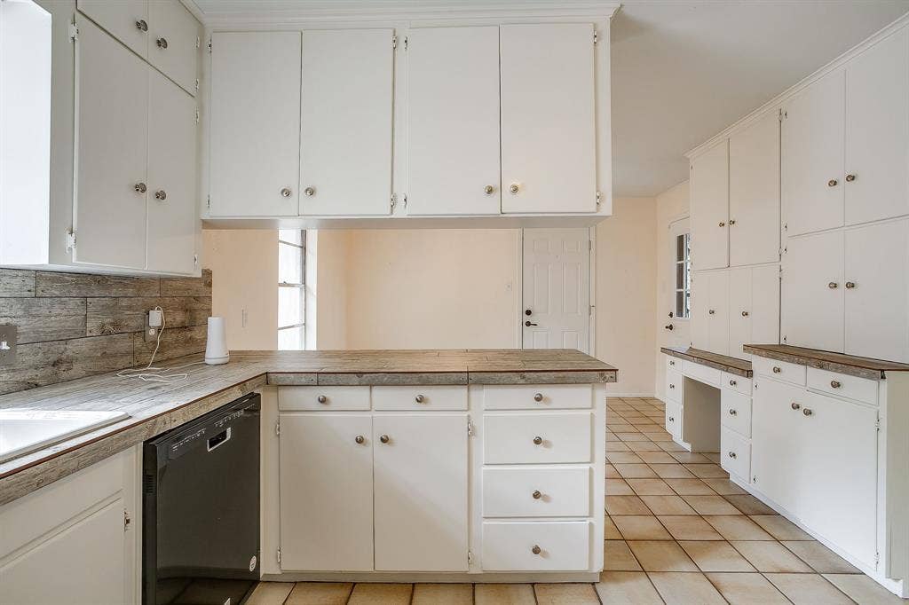 White cabinetry with silver-tone hardware, wood-finish countertops, tile backsplash, and integrated dishwasher