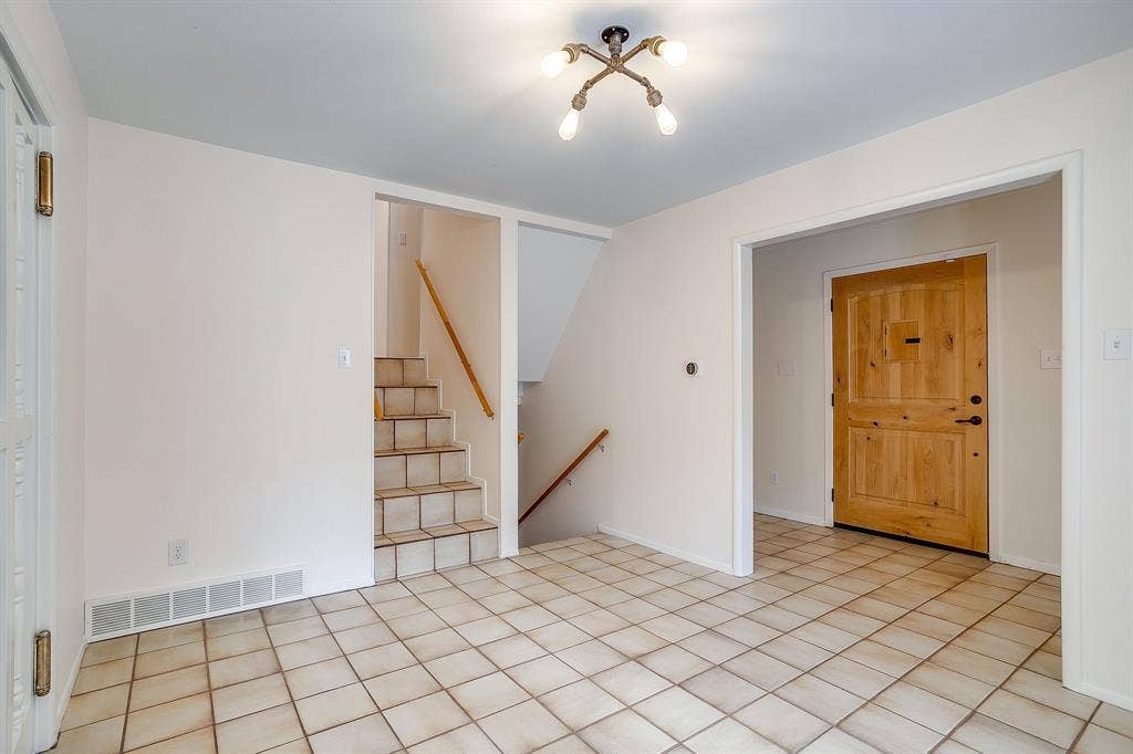 Tiled flooring, light wood-tone entry door, staircase with wood-tone railing, and a multi-bulb ceiling fixture