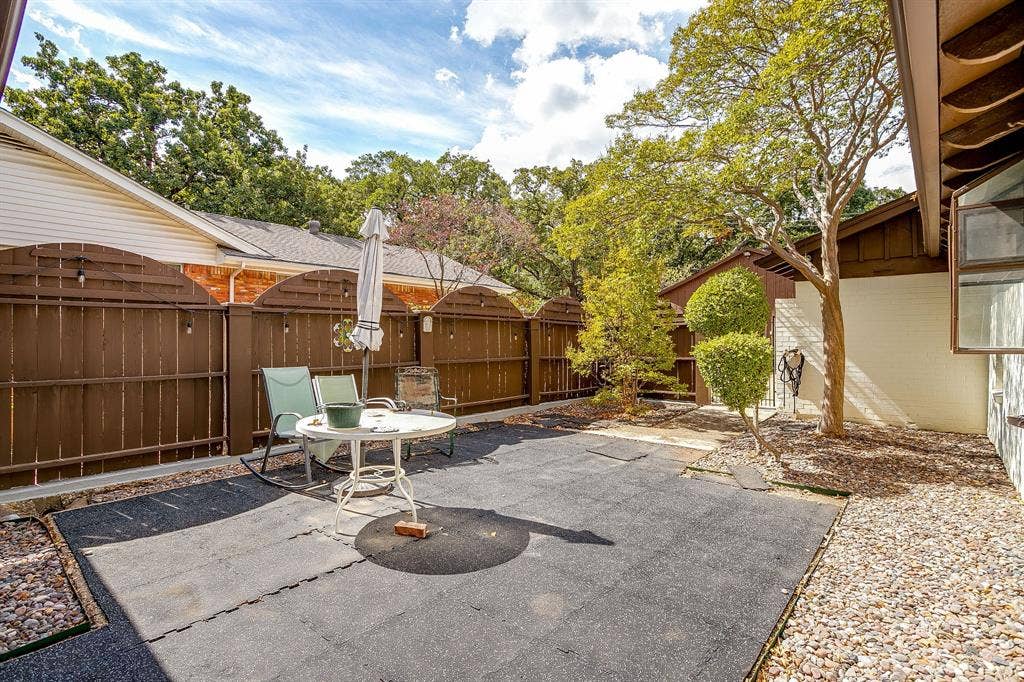 Private outdoor area featuring a dark ground surface, perimeter fencing, mature trees, and decorative gravel accents