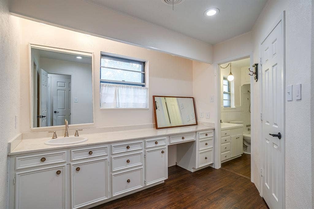 Expansive vanity with integrated sink and brass-finish faucet, ample storage cabinetry, and wood-finish flooring