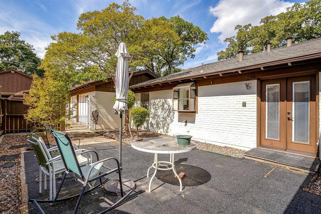Paved patio area, white brick exterior, brown trim, double glass-paneled entry doors, and a bay window