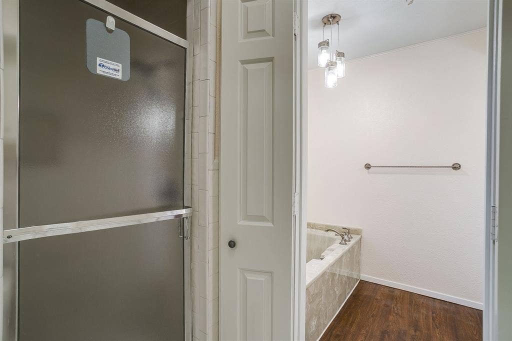 Built-in shower with textured glass enclosure, subway tile surround, deep soaking tub with stone-finish decking, wood-finish flooring, and a multi-light pendant fixture