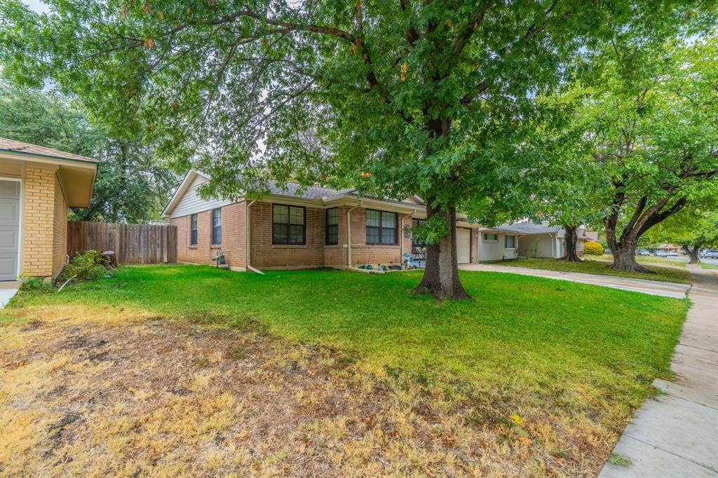 1938 Balla Way, Grand Prairie, TX 75051 Brick exterior with multiple windows, a wood fence, and mature trees