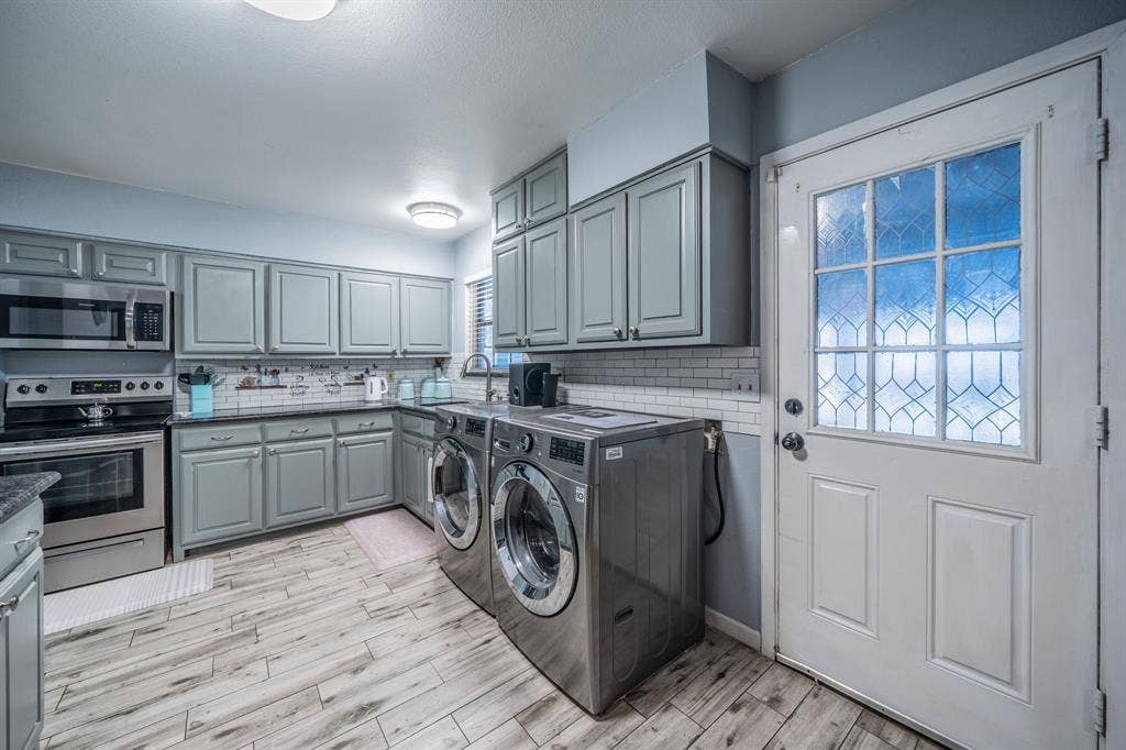 1938 Balla Way, Grand Prairie, TX 75051 Gray cabinetry with brushed nickel hardware, subway tile backsplash, stainless steel appliances, wood-finish flooring, and a decorative glass panel door