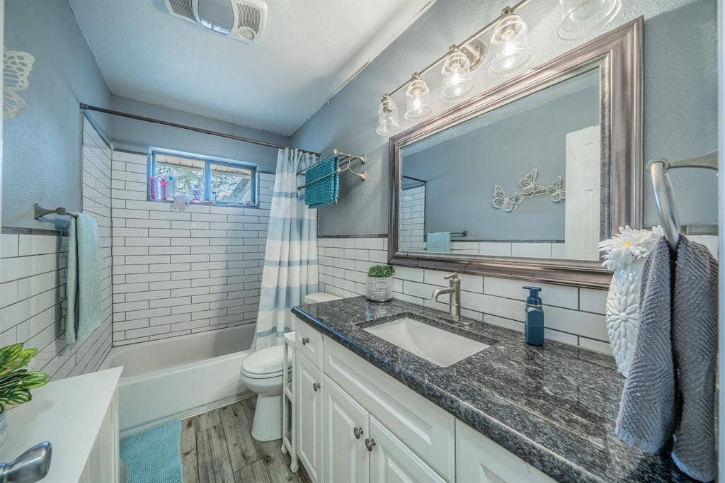 1938 Balla Way, Grand Prairie, TX 75051 Bathroom with subway tile tub surround, white vanity, dark stone-finish countertop, undermount sink, and wood-finish flooring