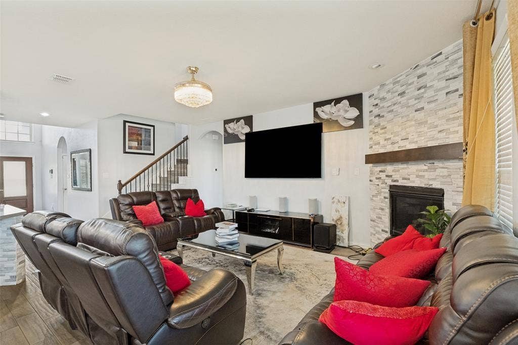 818 Black Hawk Drive, Princeton, TX 75407 Living area featuring a fireplace with a stone-tile surround, a built-in wooden mantel, wood-finish flooring, an open staircase with a wrought-iron railing, and a decorative ceiling light fixture