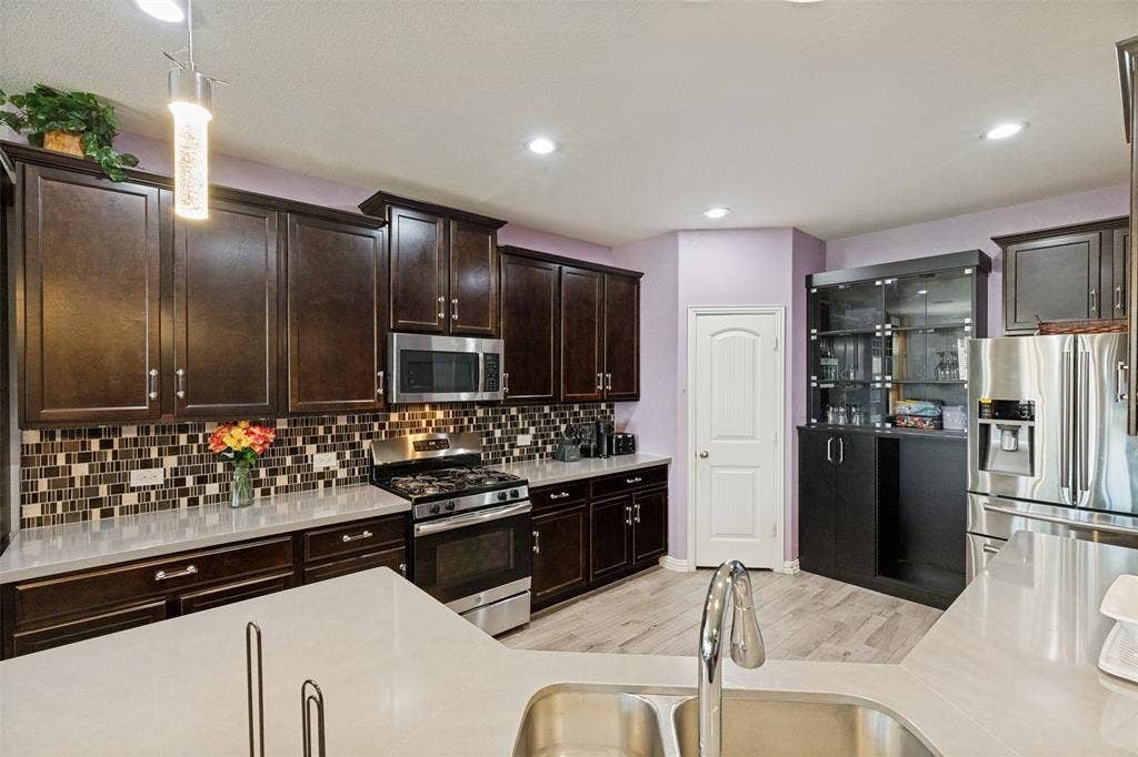 818 Black Hawk Drive, Princeton, TX 75407 Chef's kitchen featuring dark wood cabinetry, stainless steel appliances, quartz countertops, mosaic tile backsplash, and recessed lighting throughout