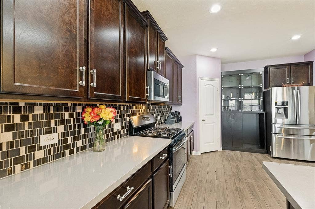 818 Black Hawk Drive, Princeton, TX 75407 Kitchen featuring wood-finish flooring, dark wood cabinetry, white countertops, and a patterned tile backsplash
