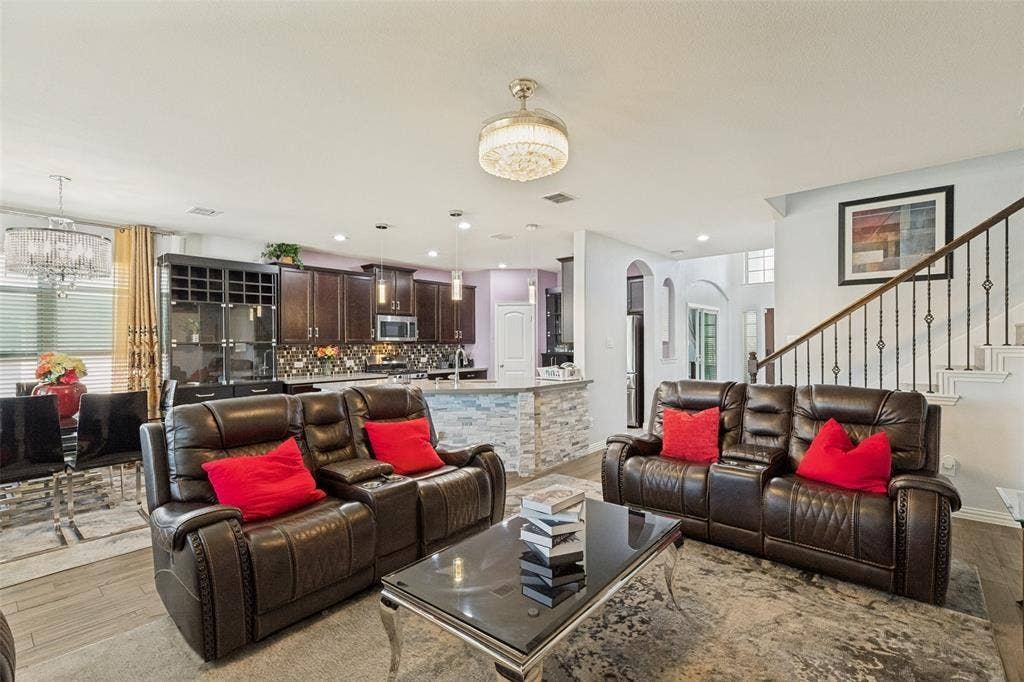 818 Black Hawk Drive, Princeton, TX 75407 Open-concept living area featuring wood-finish flooring, a kitchen with dark cabinetry, a stone-accented island, and a staircase with wrought iron balusters