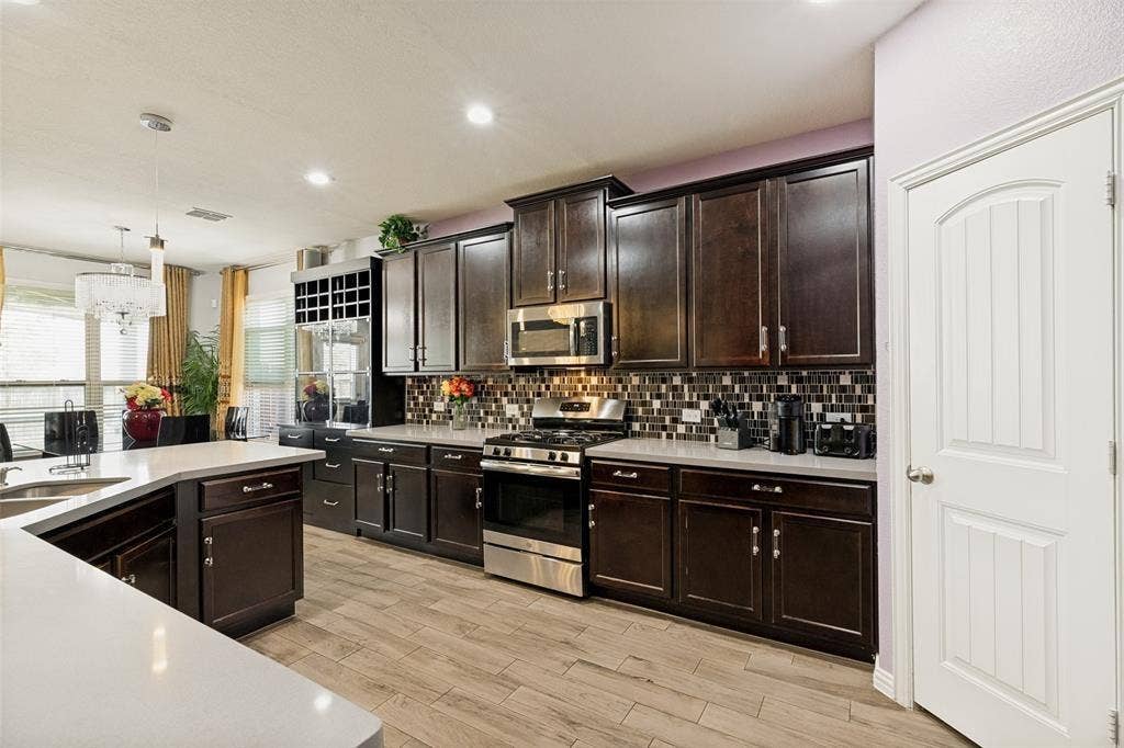 818 Black Hawk Drive, Princeton, TX 75407 Kitchen featuring wood-finish flooring, dark wood cabinetry, white countertops, a mosaic tile backsplash, and stainless steel appliances