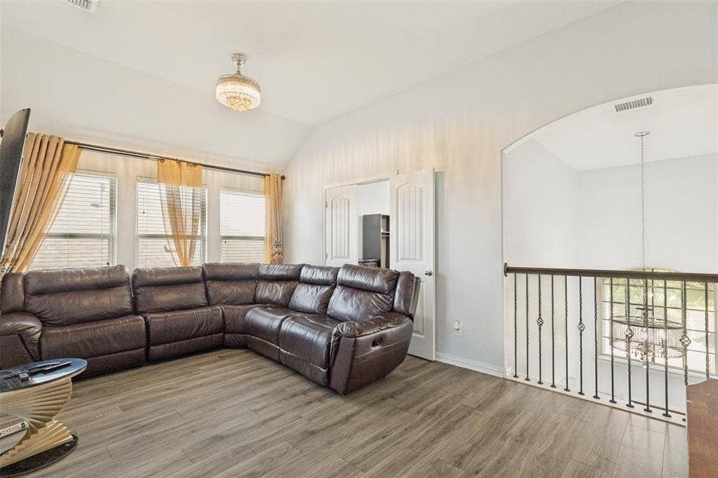 818 Black Hawk Drive, Princeton, TX 75407 Vaulted ceiling, three windows with blinds, built-in double doors, wood-finish flooring, and an ornate metal railing overlooking a lower level