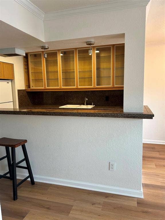 4112 Bowser Avenue, #210, Dallas, TX 75219 Breakfast bar with integrated sink, granite-style countertop, wood-finish flooring, and upper cabinetry with glass inserts