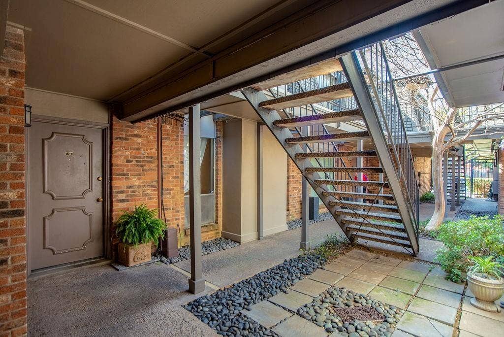 4112 Bowser Avenue, #210, Dallas, TX 75219 Brick exterior with a decorative entry door, metal staircase, and an outdoor walkway featuring stone pavers and river rock accents