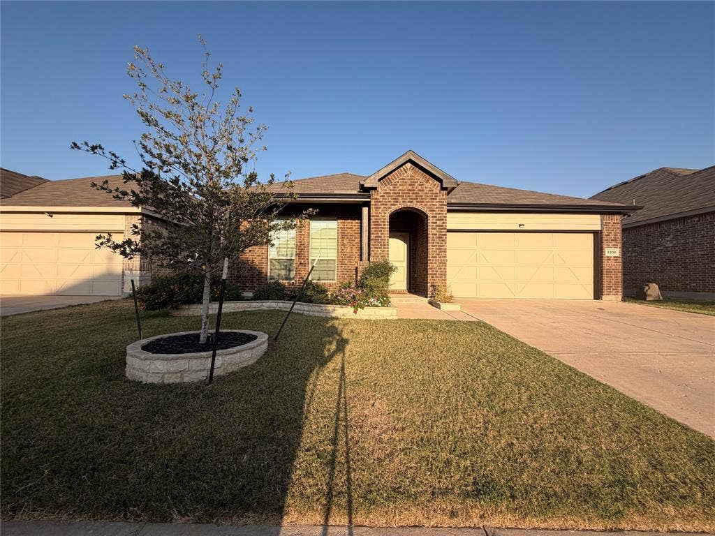 3308 Chasemoor Drive, Denton, TX 76207 Single-story brick exterior with an arched entry, two-car garage, and a planted tree in a raised stone planter