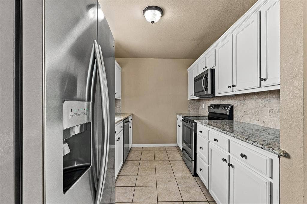624 Willow Creek Drive, Hewitt, TX 76643 Galley kitchen featuring white cabinetry, granite countertops, tile backsplash, stainless steel appliances, and tile flooring