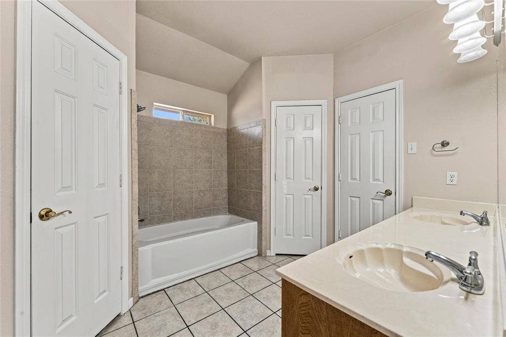 624 Willow Creek Drive, Hewitt, TX 76643 Dual vanity with integrated sinks, tiled flooring, bathtub with tiled surround, and multiple doors