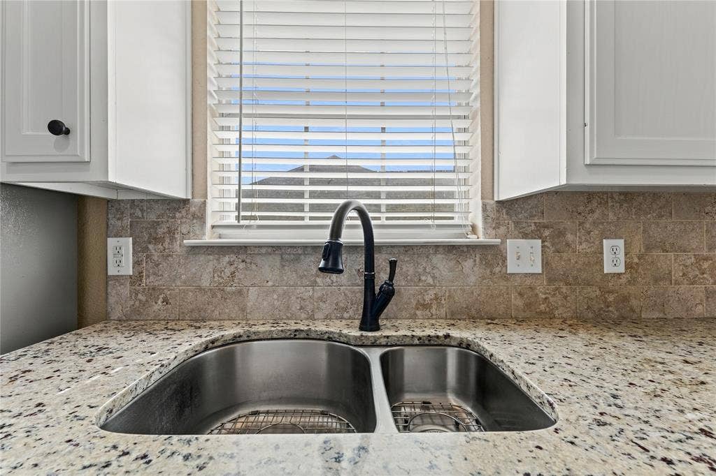 624 Willow Creek Drive, Hewitt, TX 76643 White shaker-style cabinetry with black hardware, stone-finish countertop, stainless steel double basin sink, matte black gooseneck faucet, and stone tile backsplash