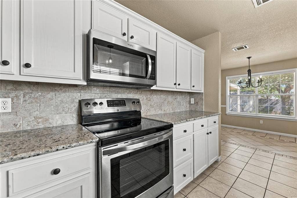 624 Willow Creek Drive, Hewitt, TX 76643 White cabinetry with dark hardware, stainless steel appliances, speckled countertops, tile backsplash, and tile flooring