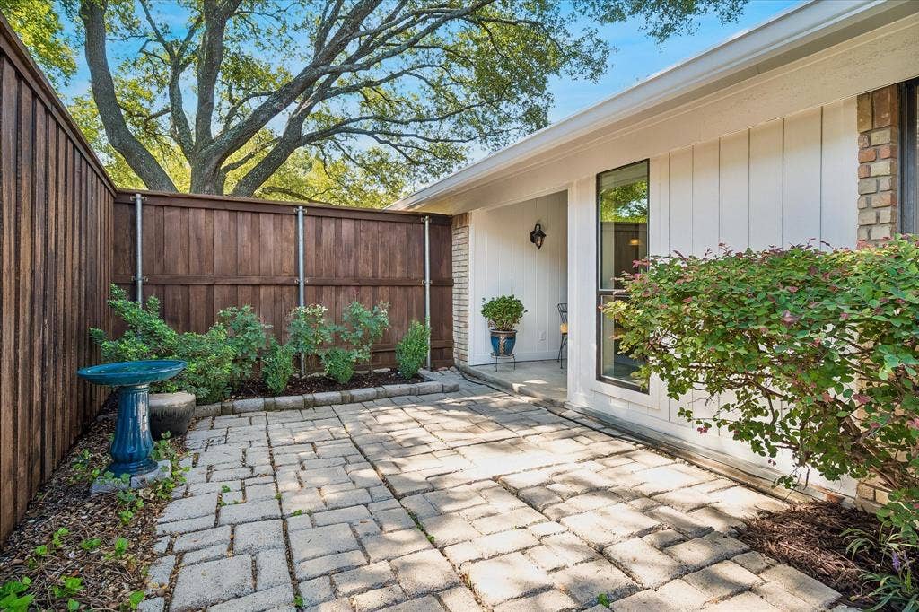 7603 Queens Ferry Lane, Dallas, TX 75248 Paved patio with decorative pavers, flanked by a full wood fence and established landscaping