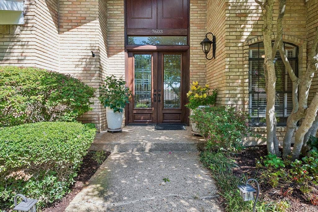 7603 Queens Ferry Lane, Dallas, TX 75248 Brick exterior with a concrete walkway, double wood-finish entry doors, transom window, and an exterior wall lantern