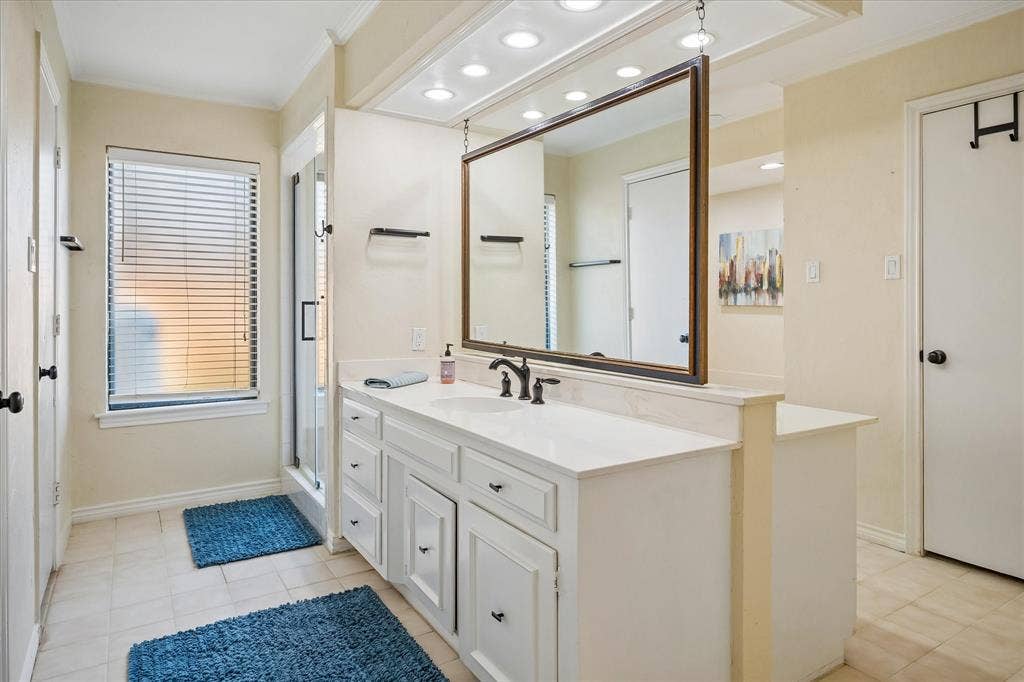 7603 Queens Ferry Lane, Dallas, TX 75248 Spacious bathroom featuring a white vanity with integrated sink, large framed mirror, tiled flooring, and a glass-enclosed shower