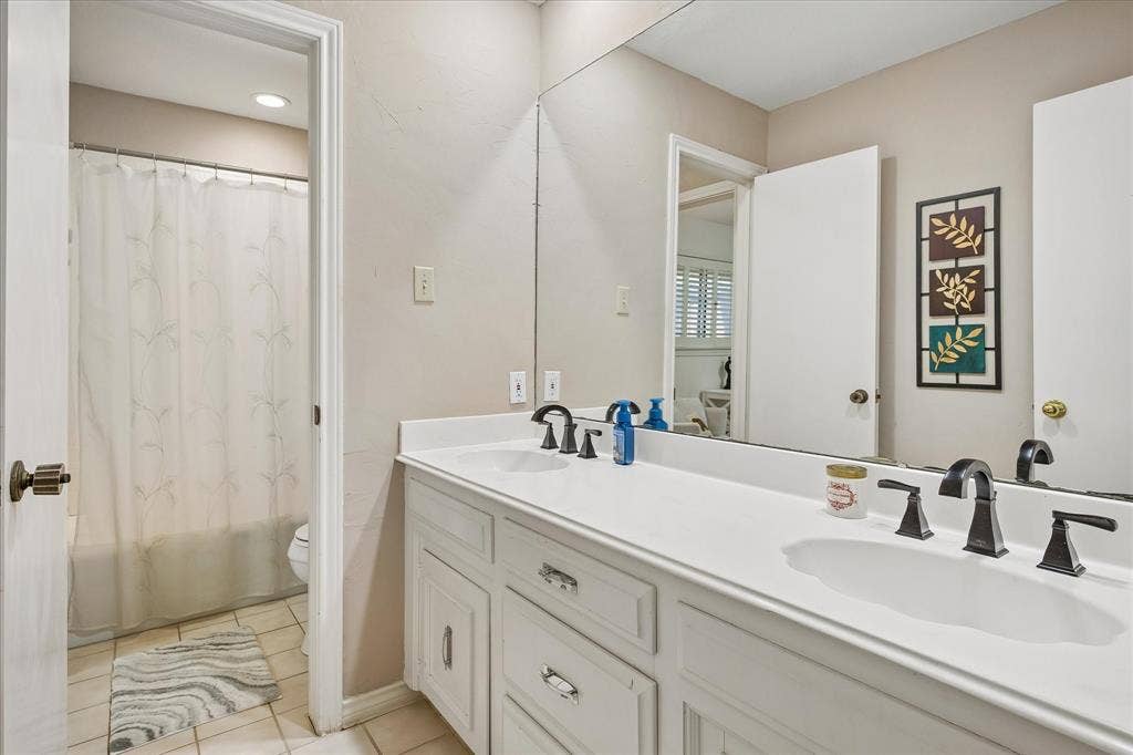 7603 Queens Ferry Lane, Dallas, TX 75248 Dual vanity with white cabinetry, solid surface countertop, and dark-finish hardware