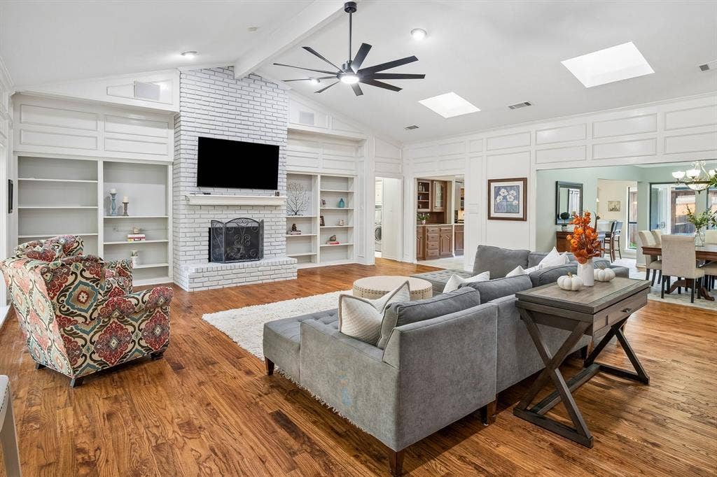 7603 Queens Ferry Lane, Dallas, TX 75248 Vaulted ceiling, wood-finish flooring, white brick fireplace, built-in shelving, and skylights
