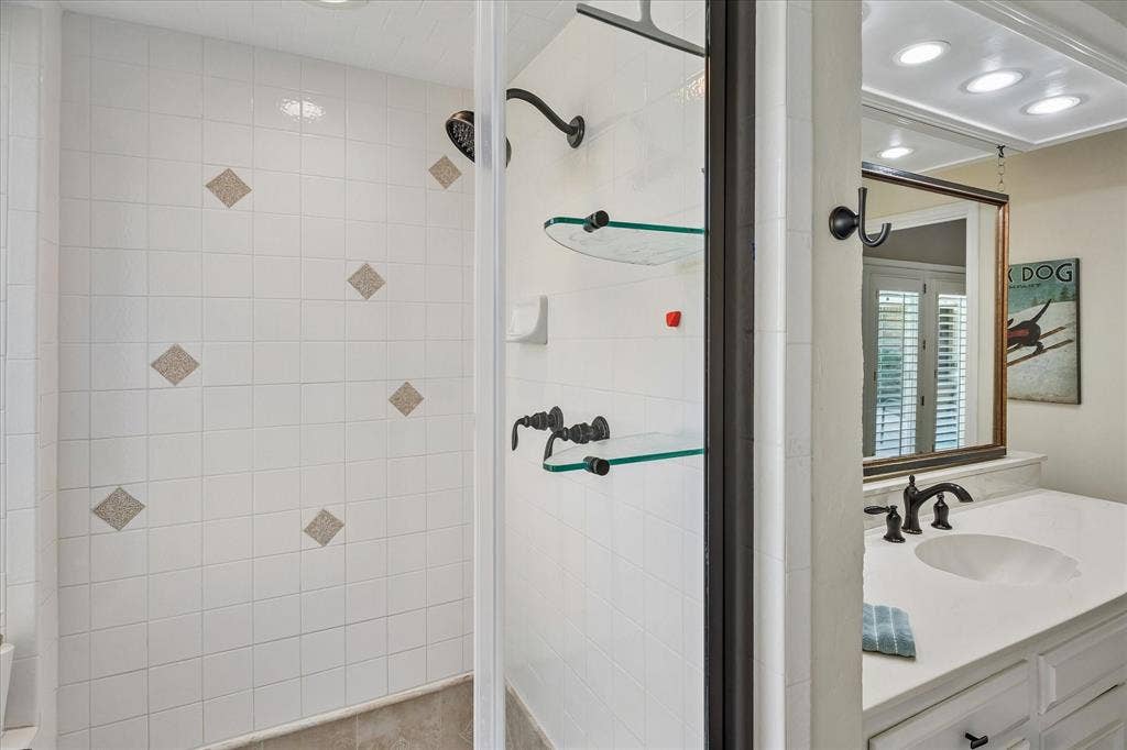 7603 Queens Ferry Lane, Dallas, TX 75248 White tiled shower with decorative accent tiles, framed glass shower enclosure, and dark bronze fixtures