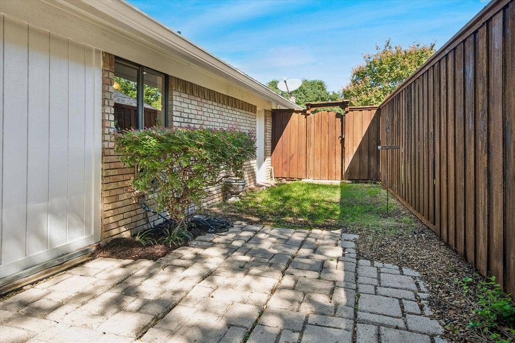 7603 Queens Ferry Lane, Dallas, TX 75248 Brick exterior with white vertical siding, established shrubbery, a paved patio, a wood privacy fence and 2nd green space