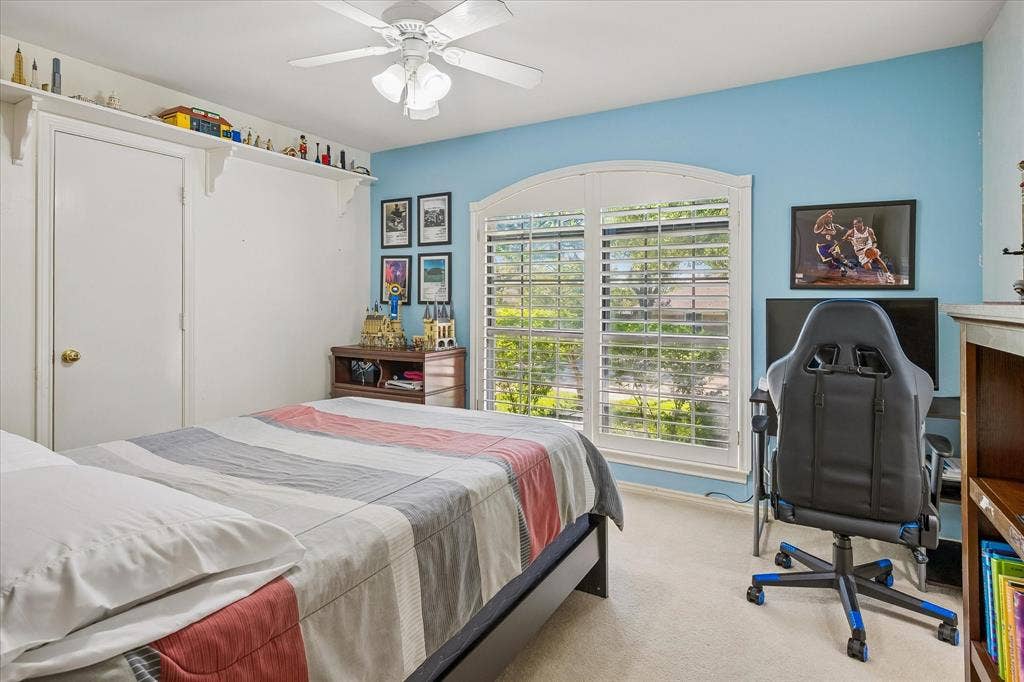 7603 Queens Ferry Lane, Dallas, TX 75248 Arched window with plantation shutters, ceiling fan, built-in shelving, and light blue accent wall