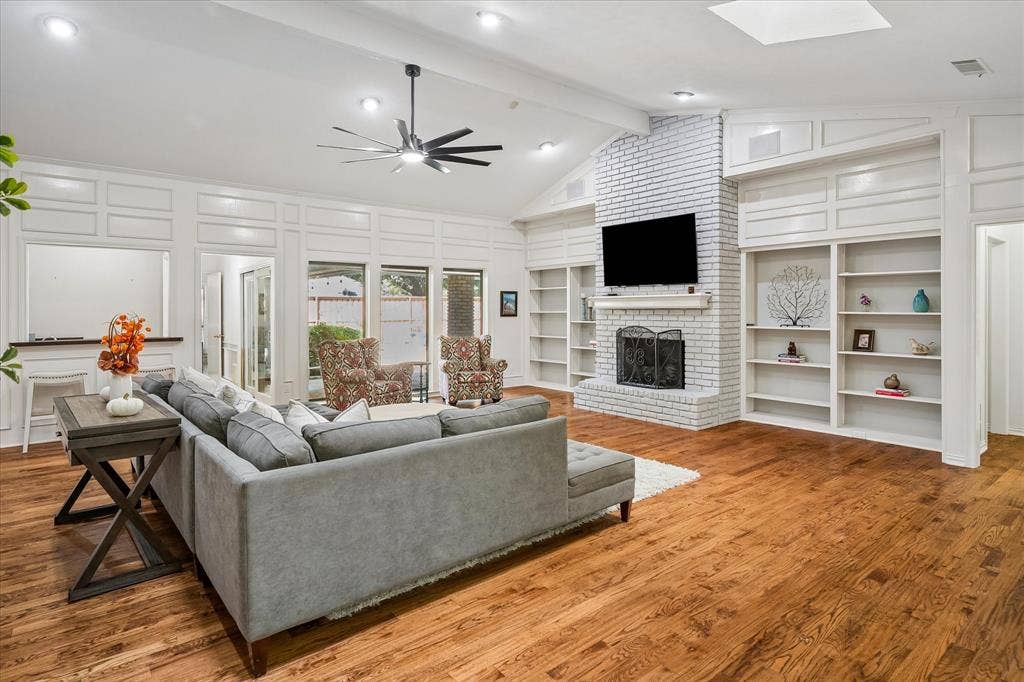 7603 Queens Ferry Lane, Dallas, TX 75248 Vaulted ceiling with a contemporary ceiling fan, wood-finish flooring, white brick fireplace with a mantel, built-in shelving, and recessed lighting