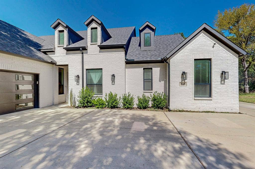 2519 Tamaron Cove, Cedar Hill, TX 75104 White brick exterior with a dark gray roof, prominent dormer windows, and a modern garage door featuring frosted panels