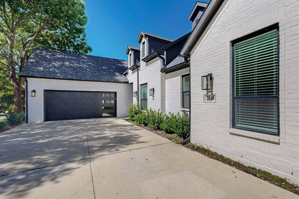 2519 Tamaron Cove, Cedar Hill, TX 75104 White brick exterior with black framed windows, a black garage door with integrated glass panels, and exterior wall lanterns