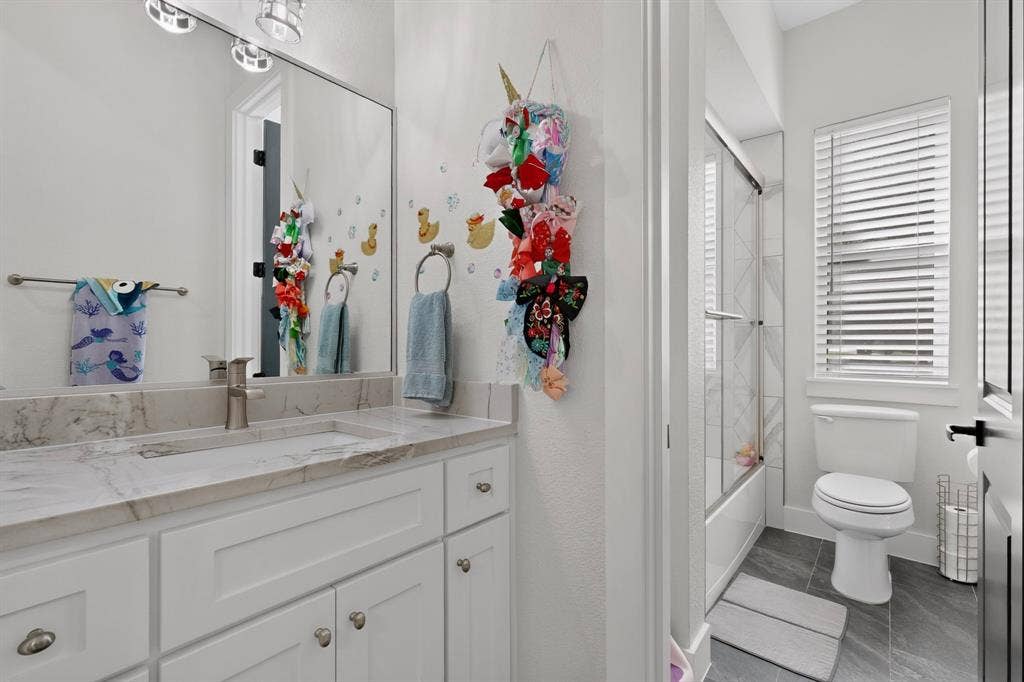 2519 Tamaron Cove, Cedar Hill, TX 75104 Bathroom featuring white shaker cabinetry, an undermount sink, a stone-finish countertop, and a shower-tub combination with a glass enclosure