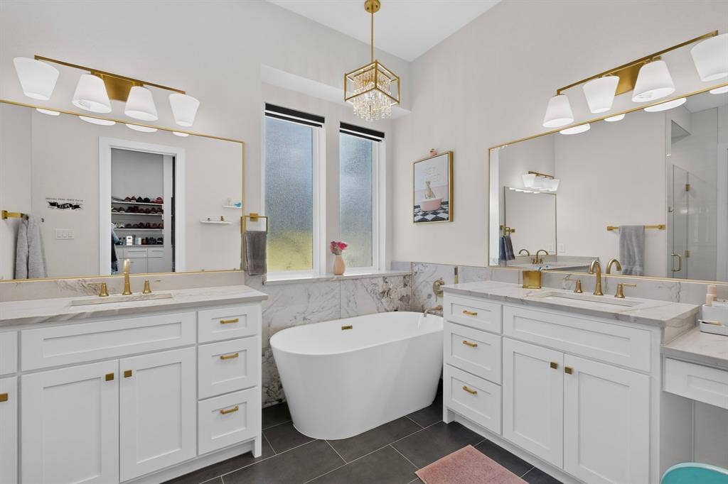 2519 Tamaron Cove, Cedar Hill, TX 75104 Dual white vanities with gold-tone hardware, a freestanding soaking tub, large format floor tile, and gold-finish lighting fixtures